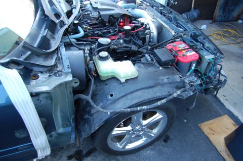 1985 Mercury Grand Marquis - Engine bay of a car with the front fender removed, revealing the battery and various engine parts.