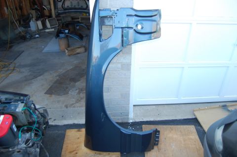 1985 Mercury Grand Marquis - A detached car fender is shown in a garage setting, with other vehicle parts visible.