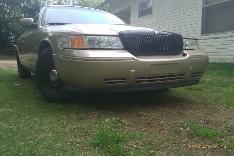 2000 Mercury Grand Marquis - A gold 2000 Mercury Grand Marquis is shown from a three-quarter front view, parked outdoors on a grassy area.