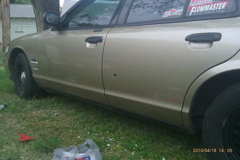 2000 Mercury Grand Marquis - Side view of a gold sedan showing a bullet hole in the door and aftermarket stickers on the rear window.