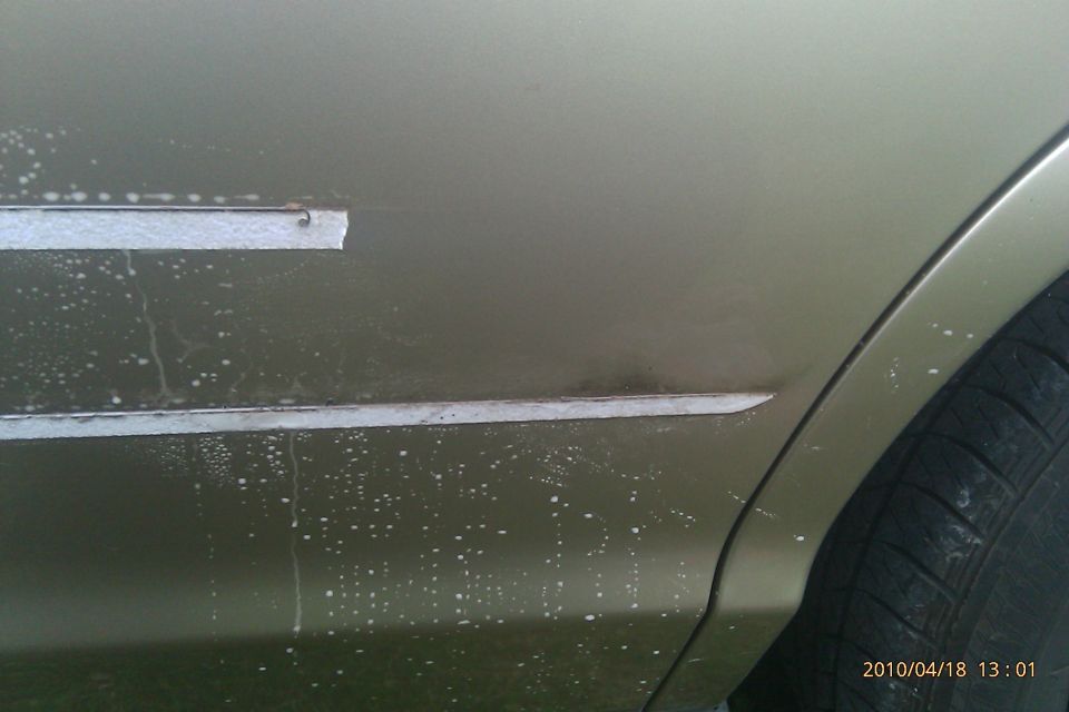 Gold car door with two horizontal chrome trim pieces, one detached, and water spots