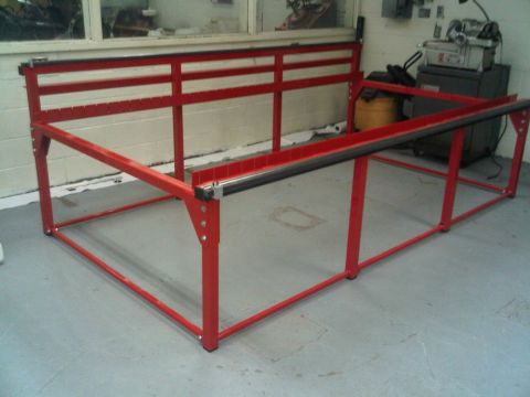 1996 Ford Bronco - A red metal frame structure with black rails and a cutting guide is positioned on a workshop floor.