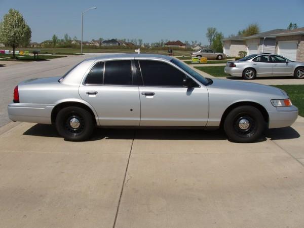 Silver sedan parked on a driveway. Another silver sedan and a tan car are in the background