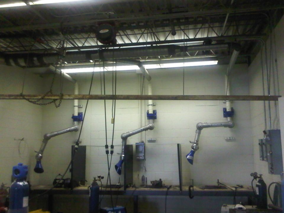 Three articulated fume extractors hang from ceiling pipes above a workbench in a workshop