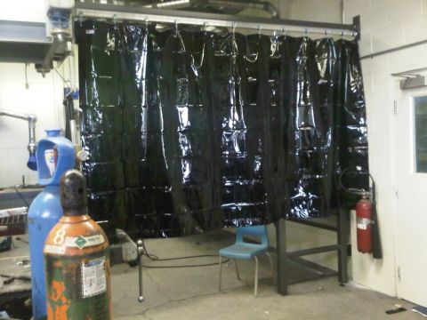 1996 Ford Bronco - A welding station is set up with a protective curtain and gas cylinders, ready for use.