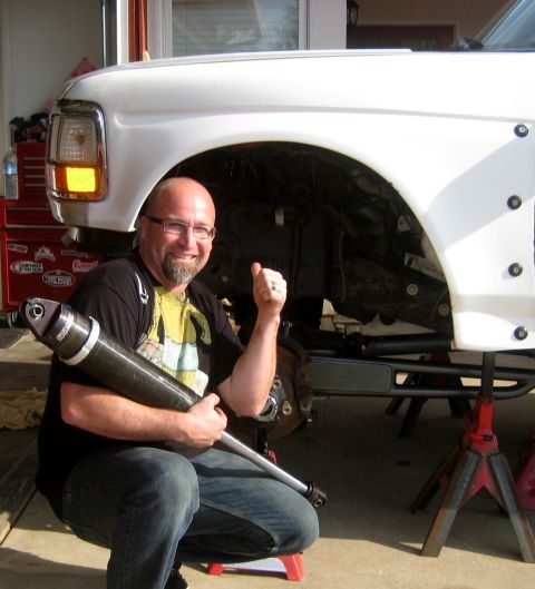 1996 Ford Bronco - A man holds a new shock absorber next to the front suspension of a white 1992 Ford F-150.