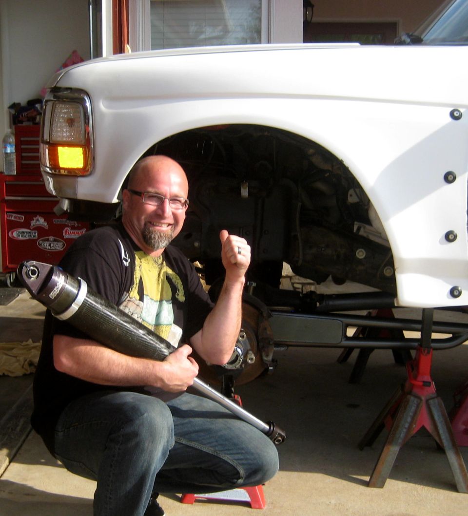White 1992 Ford F-150 front suspension with a man holding a shock absorber