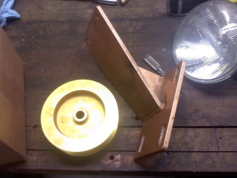 1992 Ford Bronco - Pulley and bracket on workbench with a headlight visible.