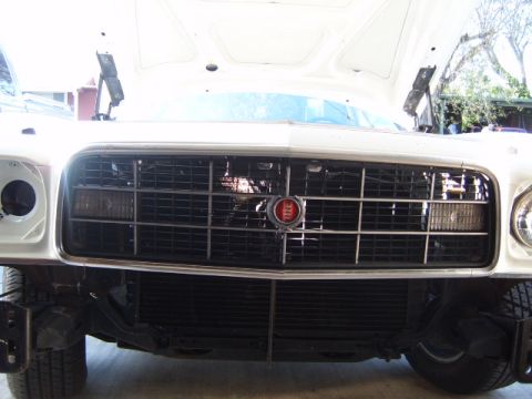 1973 Ford Ranchero - Front view of a white car's grille, a red emblem and horizontal bars, with the hood open.
