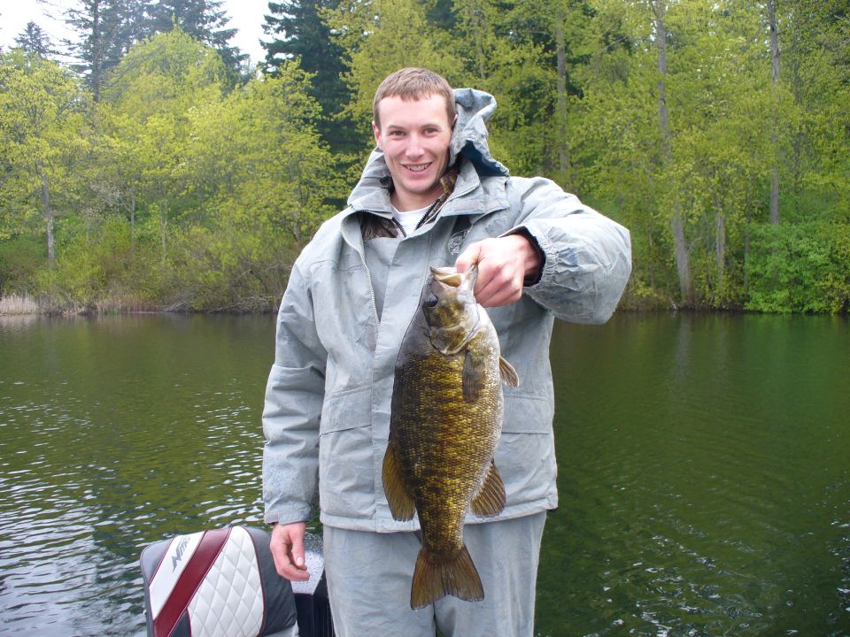 Angler in a bass boat holding up a smallmouth bass on a tree-lined lake