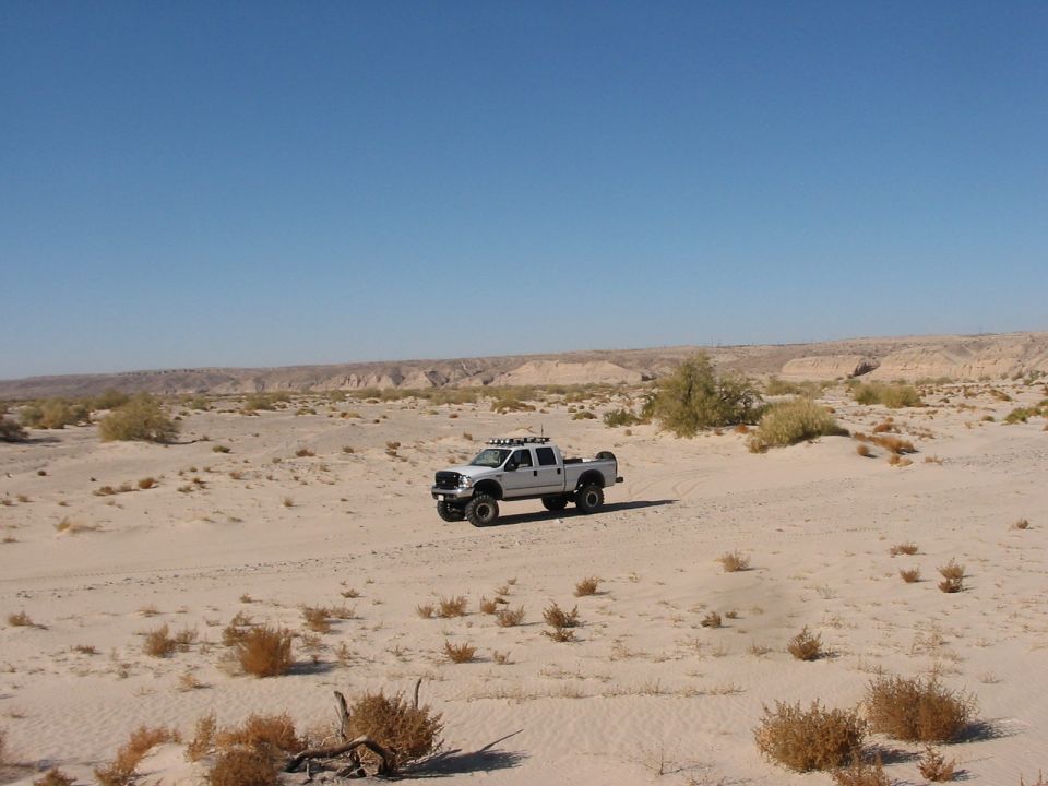 White lifted crew-cab Ford pickup with roof lights parked in a sandy desert wash