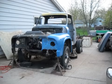 1954 Ford F-100 - A partially disassembled 1953 Ford F-100 truck is elevated on jack stands in a driveway, awaiting restoration.