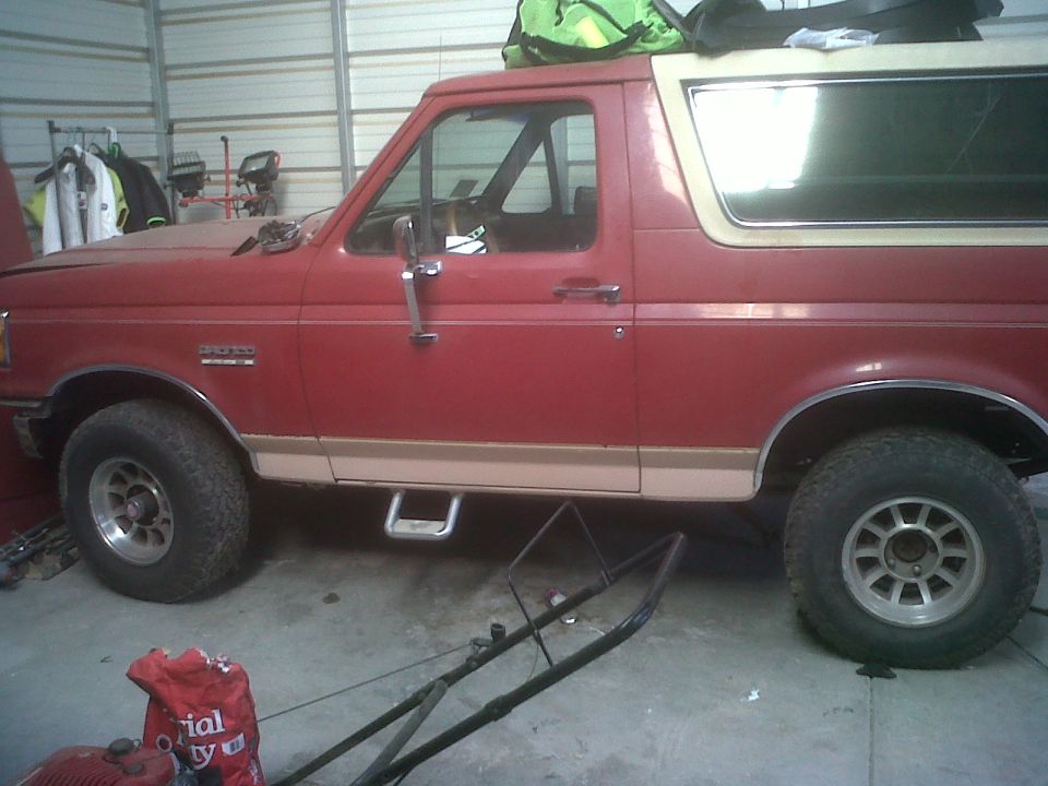 Red Ford Bronco with tan trim, side view, in a garage with a lawnmower