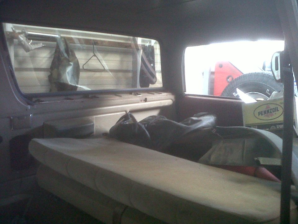 Interior view of a vehicle, showing seats, stored items, and a spare tire visible through a side window
