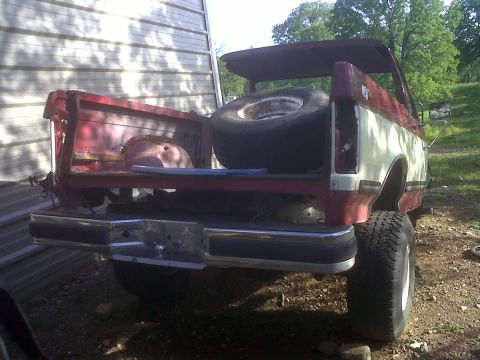 1989 Ford Bronco - The rear of a pickup truck shows its bed, bumper, and spare tire, with a building in the background.