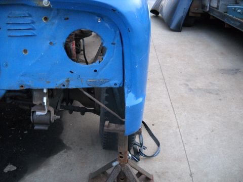 1954 Ford F-100 - Close-up of a blue truck's front fender and wheel well area, showing suspension components and the vehicle on jack stands.