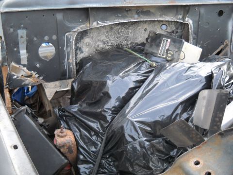 1954 Ford F-100 - The engine bay of a 1954 Ford F-100 is obscured by trash bags and debris.