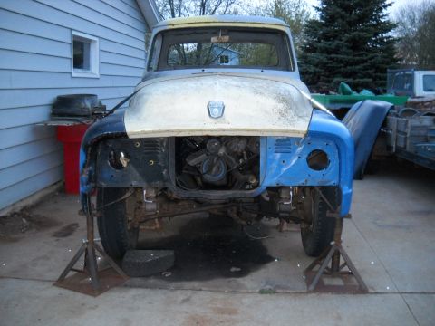 1954 Ford F-100 - This disassembled 1953 Ford F-100 truck is on jack stands, showing its exposed engine and missing front end components.