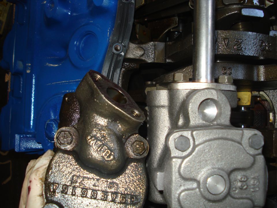 Close-up of engine parts, including a blue block and metal components. Part numbers are visible on one piece