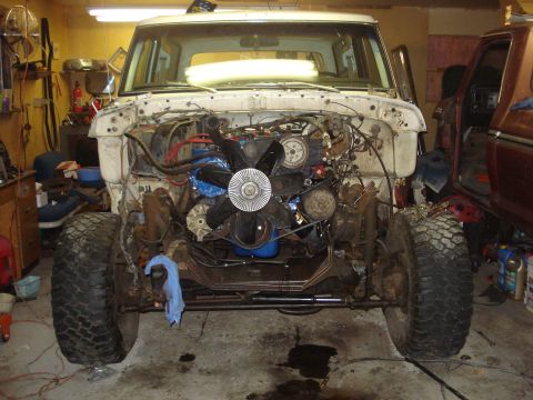 1979 Ford Bronco - A white Ford Bronco sits in a garage with its front end removed, revealing the engine and suspension components.