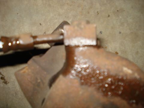 1979 Ford Bronco - Close-up of a rusted brake caliper part with a metal line attached.