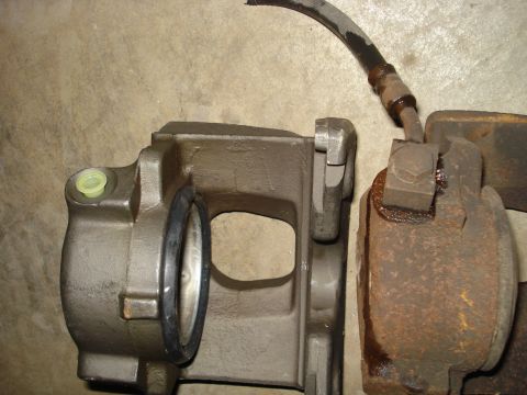 1979 Ford Bronco - A comparison of a new brake caliper next to a heavily rusted one, with a brake hose attached to the rusted component.