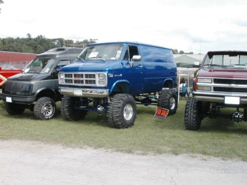 1994 Ford Bronco - Several modified vehicles, including a lifted blue GMC van, are displayed on a grassy field.