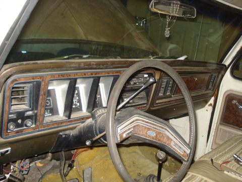 1979 Ford Bronco - Driver's-side interior view of a torn-down square-body Ford dash with woodgrain trim, a two-spoke steering wheel with Ford emblem, column s…