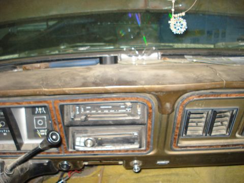 1979 Ford Bronco - Close-up of a brown late-1970s Ford truck dashboard with woodgrain trim, showing the slide-lever heater controls, an aftermarket CD head un…