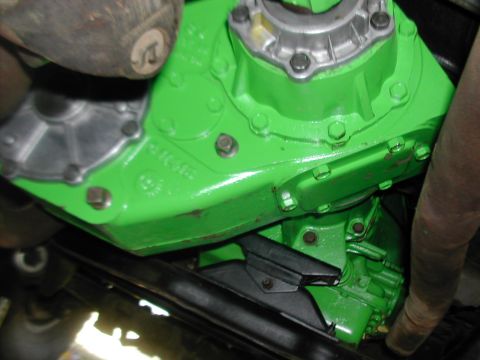 1979 Ford Bronco - Close-up of a green painted transfer case and exhaust pipe, likely from a vehicle's drivetrain.
