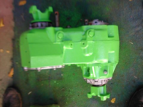 1979 Ford Bronco - Cast-iron gear-driven transfer case freshly painted bright lime green, laid on its side on green-overspray-covered ground with autumn leave…