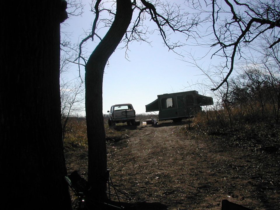 White lifted truck parked next to a pop-up tent camper at a dirt campsite