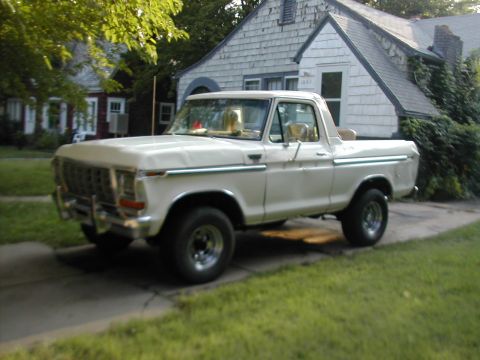 1979 Ford Bronco - Three-quarter front view of a white late-1970s Ford Bronco with the top removed, parked on a driveway in front of a shingled house. It wear…