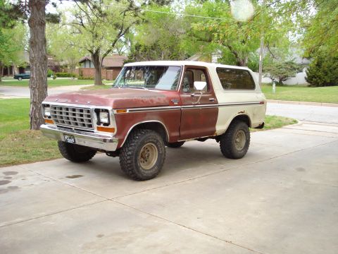 1979 Ford Bronco - Three-quarter front view of a two-tone maroon-and-cream late-1970s Ford Bronco with a removable hardtop, sitting lifted on aggressive mud-t…