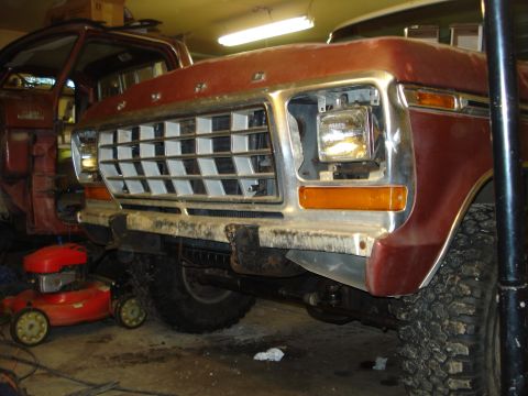 1979 Ford Bronco - Low three-quarter front shot of a maroon late-1970s Ford truck in a garage with the grille and headlight bezels partly disassembled, one he…