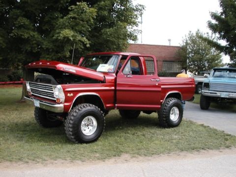 1994 Ford Bronco - Red 1967 Ford F-series pickup truck with hood open, parked on grass next to a blue truck.