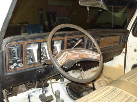 1979 Ford Bronco - Interior view from the driver's door of an older Ford, showing the two-spoke steering wheel with a 'Ford' emblem, woodgrain-trimmed dashboa…