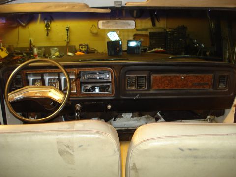 1979 Ford Bronco - Interior of a late-1970s Ford truck shot from behind the front bucket seats, showing a brown dash with woodgrain trim, tan four-spoke steer…