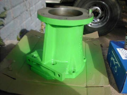 1979 Ford Bronco - Cast adapter housing painted bright green, resting on cardboard on a garage floor with its machined mounting flange and pilot bore masked o…