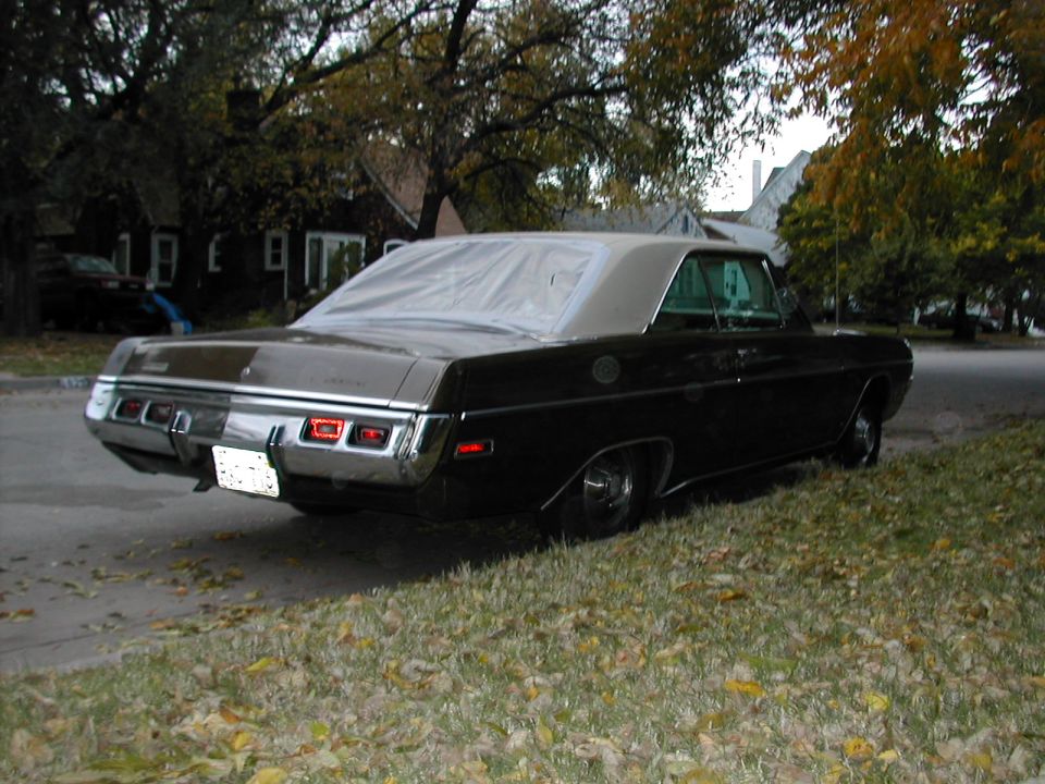 Black 1970 Dodge Dart parked on grassy shoulder, rear view. Covered roof