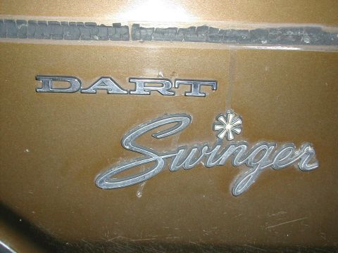 1971 Dodge Dart - Close-up of Dodge Dart Swinger emblems on a gold car body. Cracked trim is visible above.