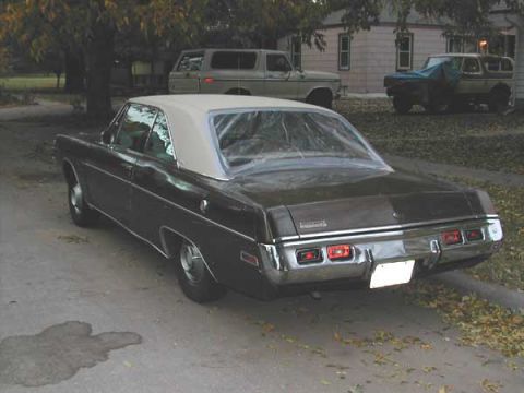 1971 Dodge Dart - A dark-colored sedan with a white vinyl top is parked on a street, with other vehicles and houses visible in the background.