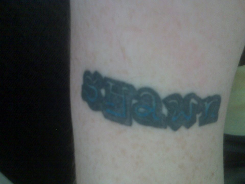 Tattoo of the word 'slam' in blue graffiti-style lettering on skin