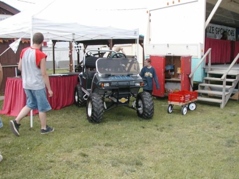 1994 Ford Bronco - A modified golf cart with oversized tires sits on display outdoors near a trailer and a tent.