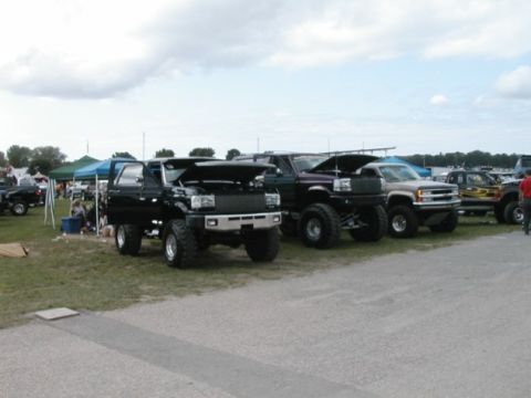 1994 Ford Bronco - A lifted 1994 Ford Bronco is parked with its hood open alongside other modified trucks and SUVs.