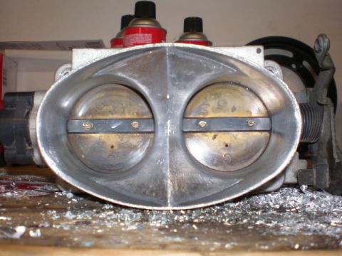 2007 Ford Mustang - A dual throttle body sits on a workbench, surrounded by metal shavings.