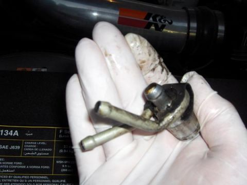 2007 Ford Mustang - Close-up of a fuel injector part being held by a gloved hand, with a K&N intake tube in the background.