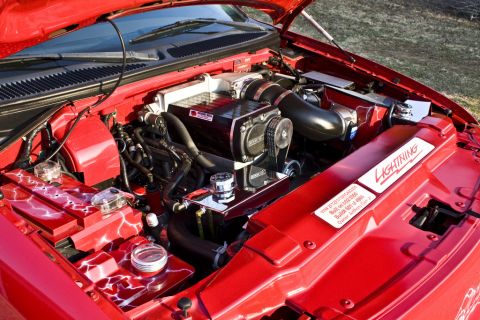 2007 Ford Mustang - The engine bay of a vehicle is shown with a supercharger and custom red paint with lightning bolt accents.