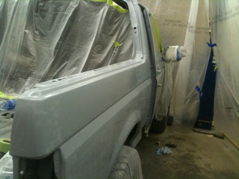 1993 Ford Bronco - A vehicle body is being prepped for painting inside a spray booth, covered in plastic sheeting.