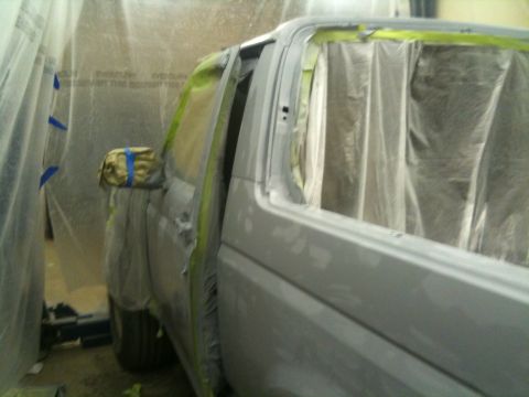 1993 Ford Bronco - A gray Ford Bronco is prepped for painting inside a booth, with its door ajar and windows covered.